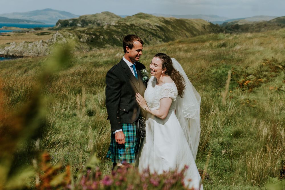 A Scottish highland wedding photo with the newlyweds posing on green rolling hills.