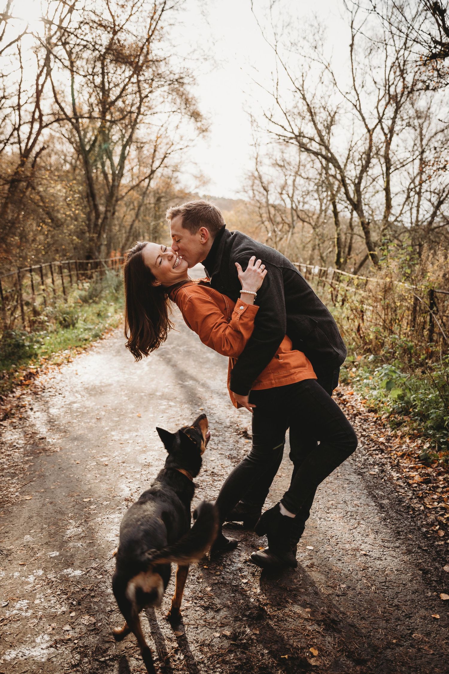 Romantic couple sharing playful moment on autumn trail with their dog watching.