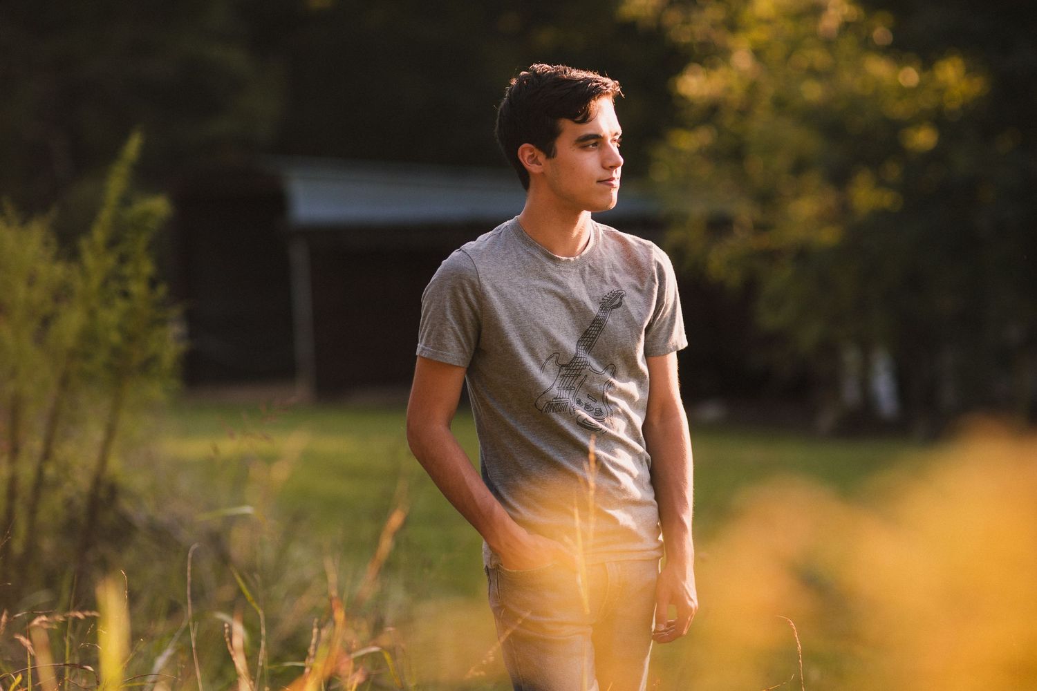 Casual portrait in grey t-shirt standing in sunlit field during golden hour.