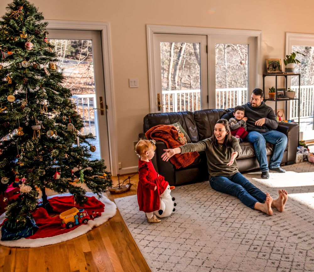 Living room decorated for Christmas with tree while family relaxes on sofa.