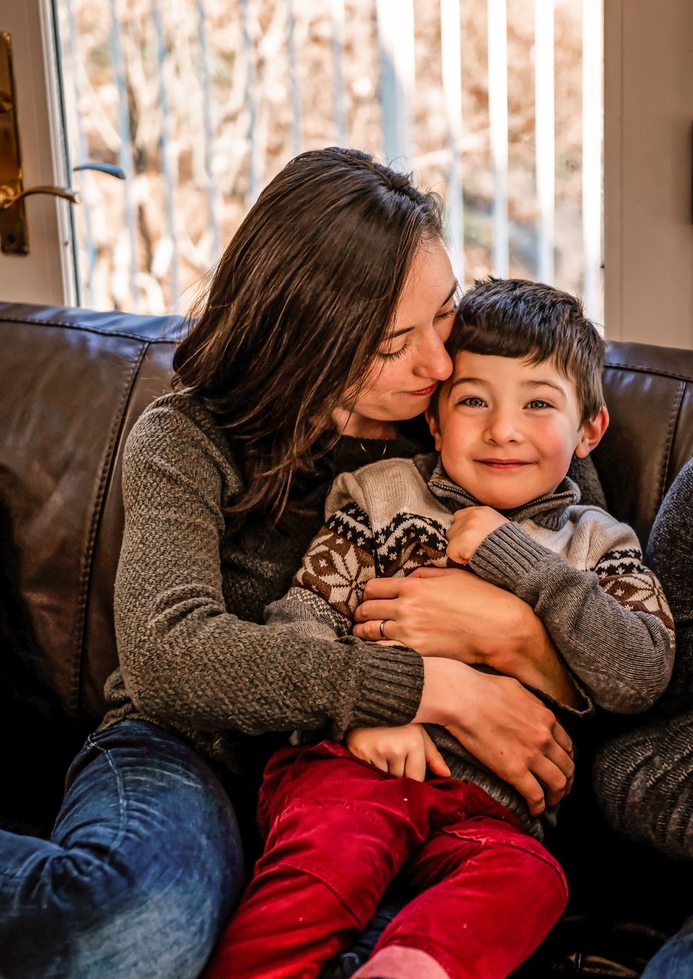 Tender moment between parent and child cuddling on cozy leather couch.