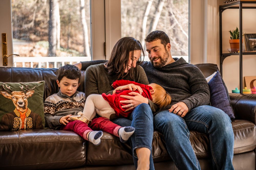 Family relaxes together on brown leather couch during cozy afternoon at home.