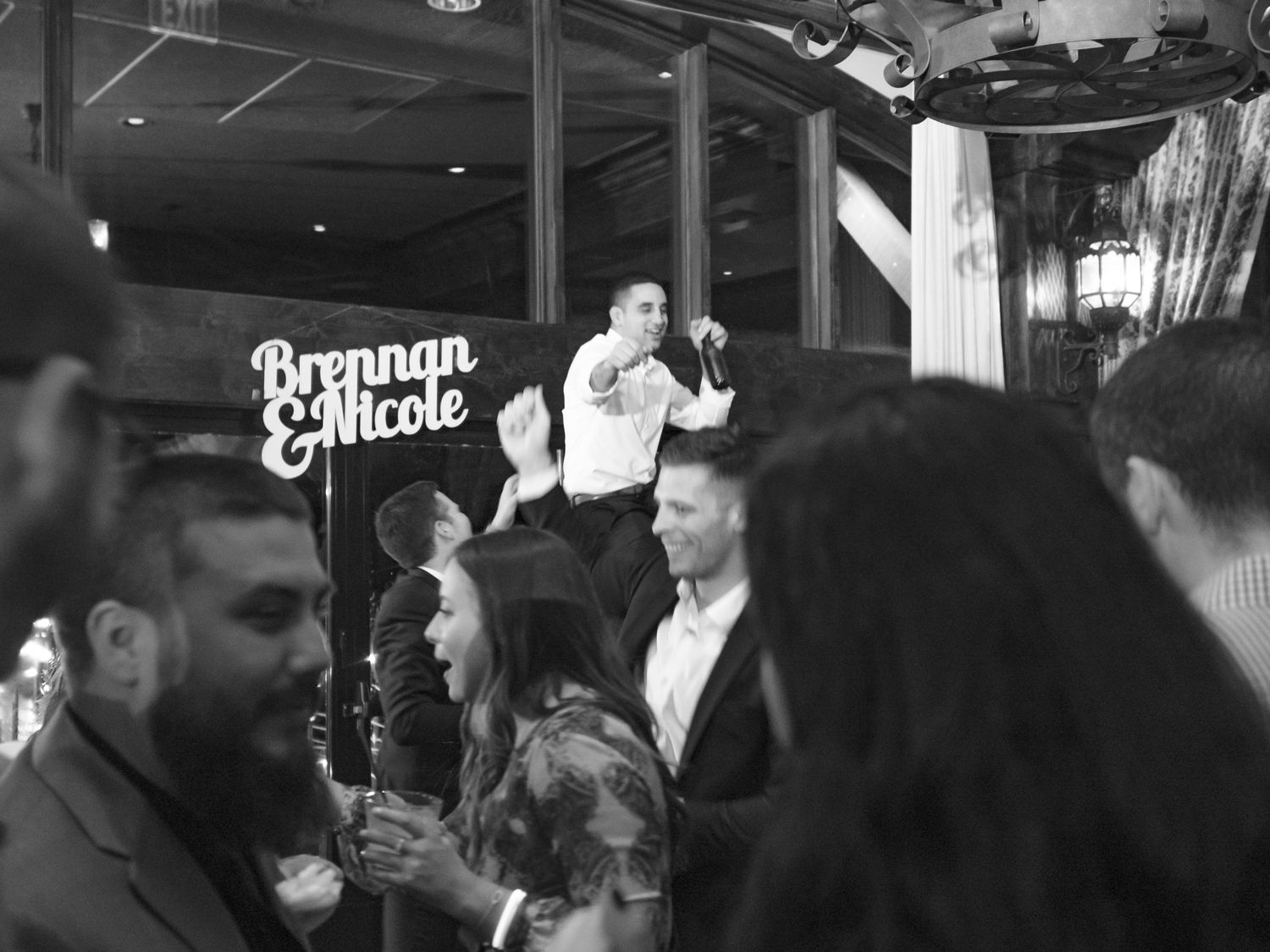 A black and white crowded bar scene shows a performer energetically entertaining from an elevated position above the audience.