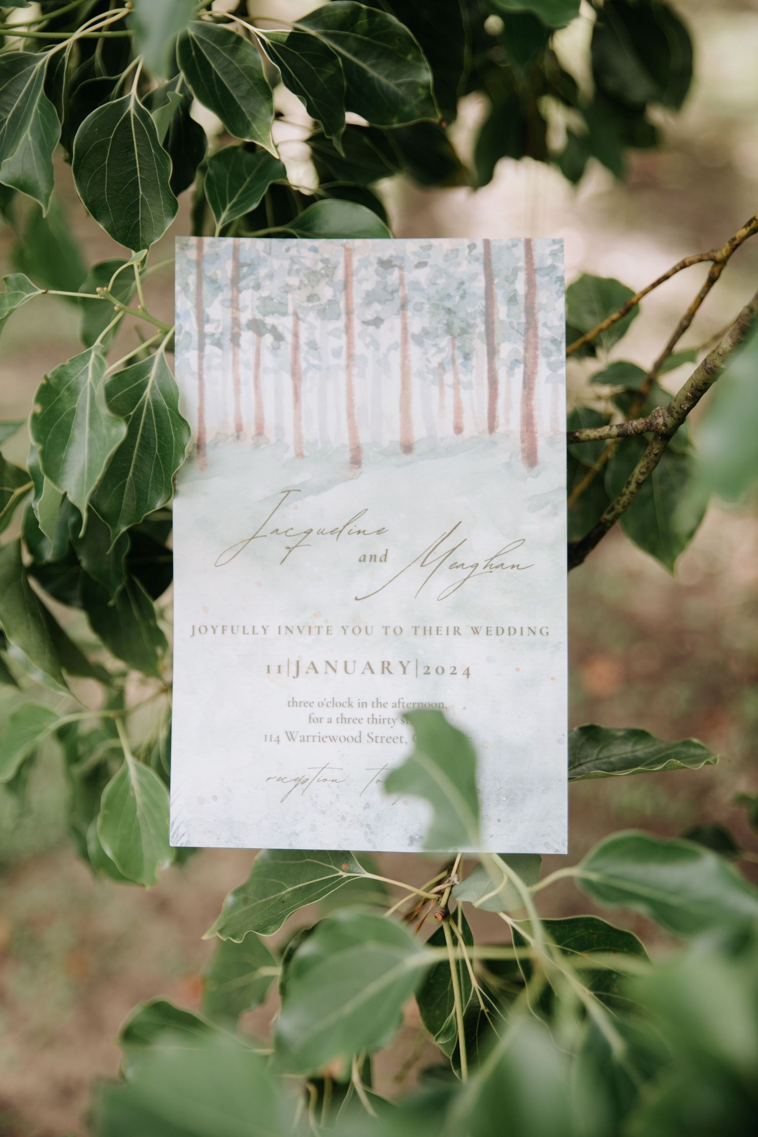 Wedding invitation with watercolor forest design nestled among green leaves.