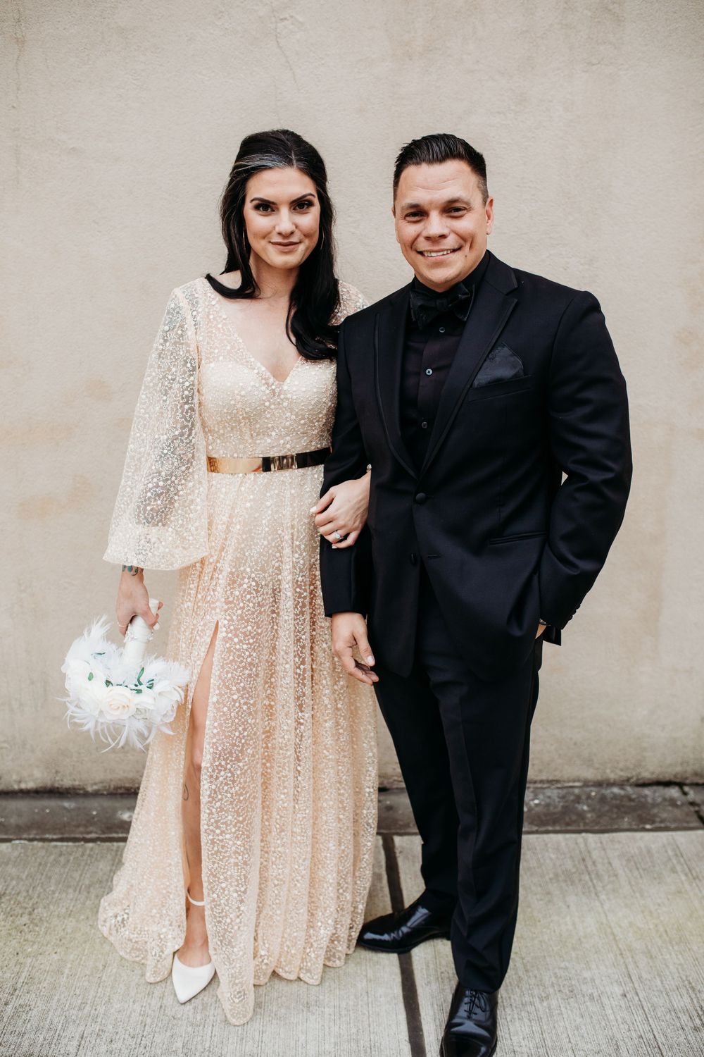 Bride in sparkly champagne gown with groom in black suit posing together at wedding celebration.