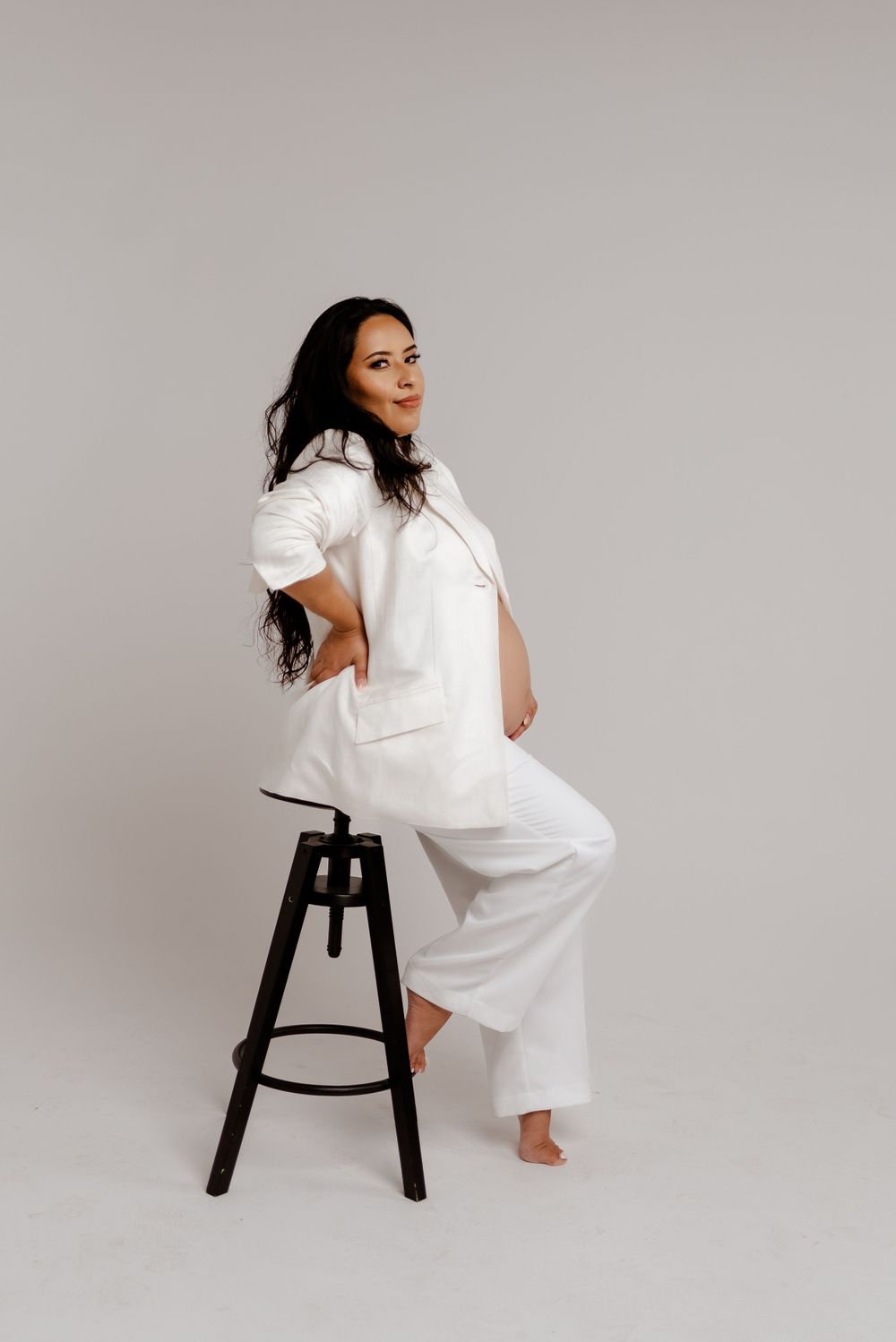 White backdrop studio maternity, luxury maternity, model wears white blazer and golden necklace.