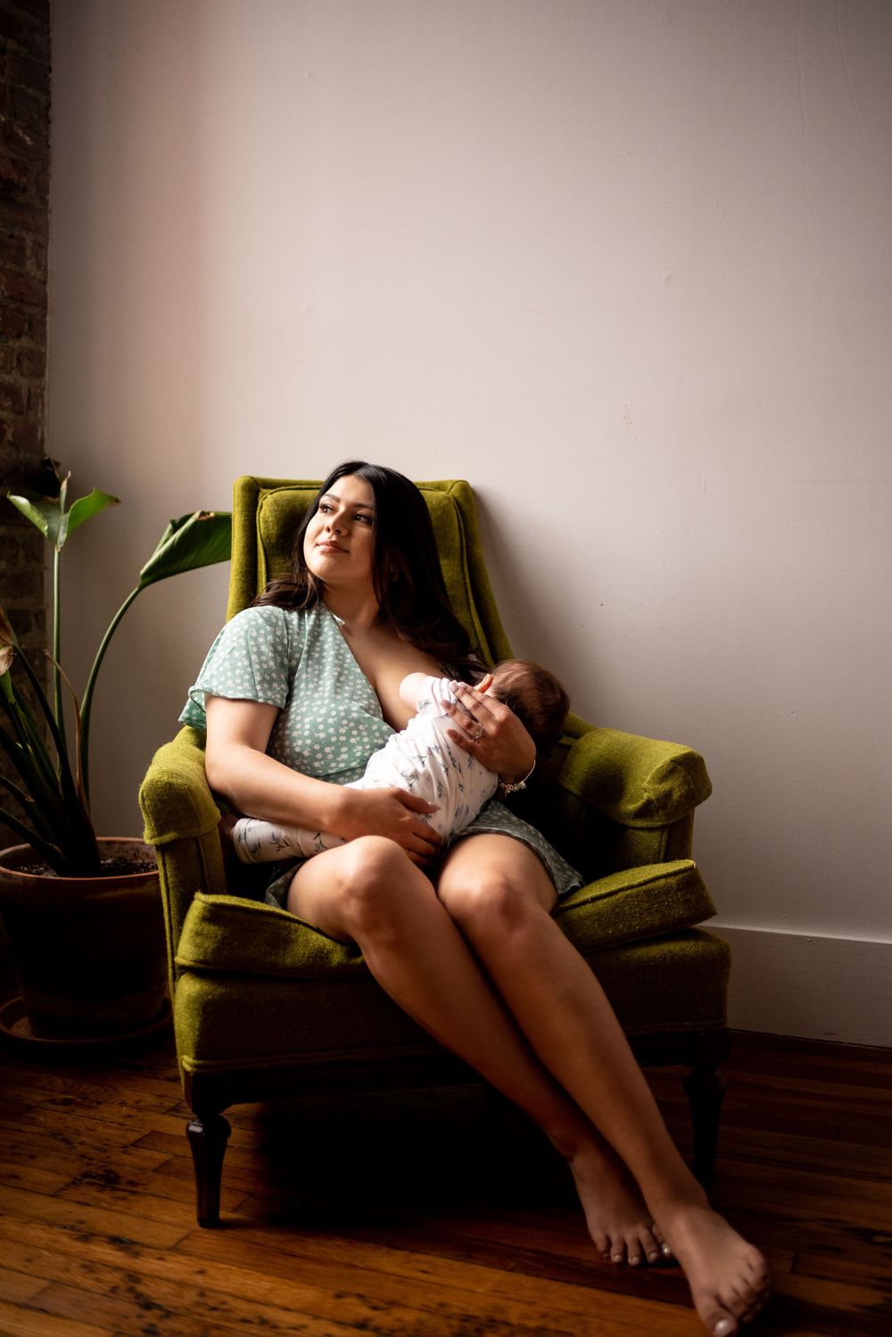 Breastfeeding photoshoot with mother and baby by the window, natural light studio.