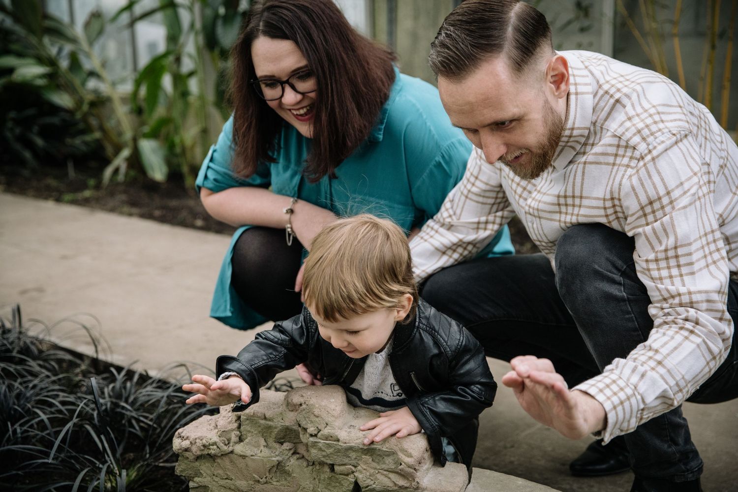 Family kneeling together to examine something interesting in the greenhouse soil.