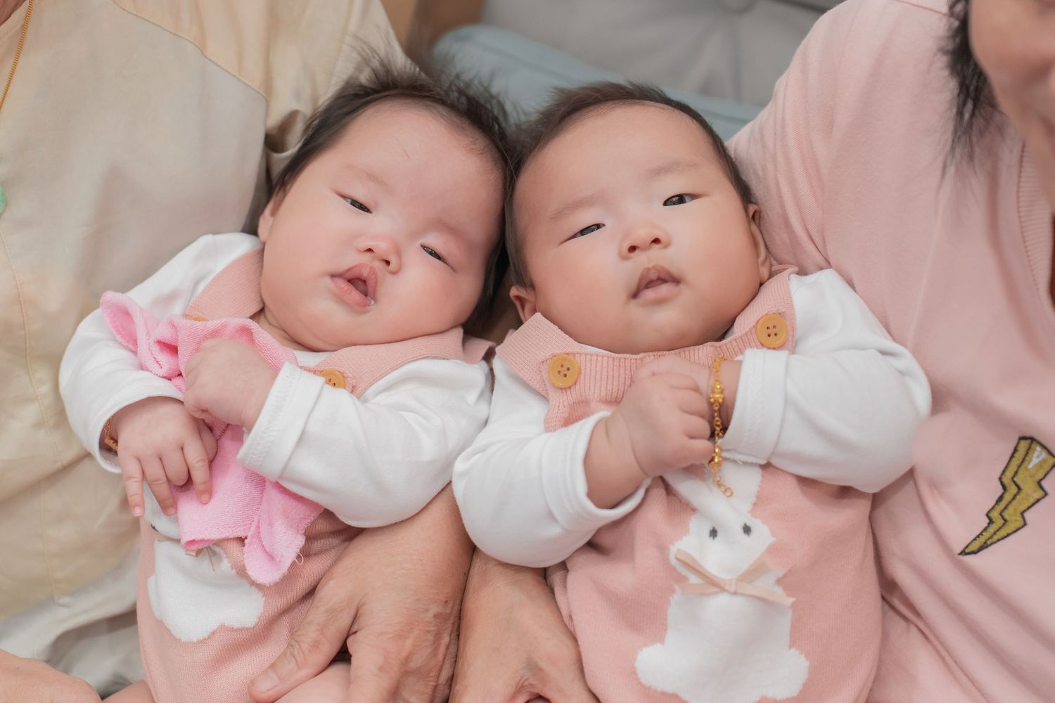 Two adorable Asian babies in pink and white onesies lying side by side.