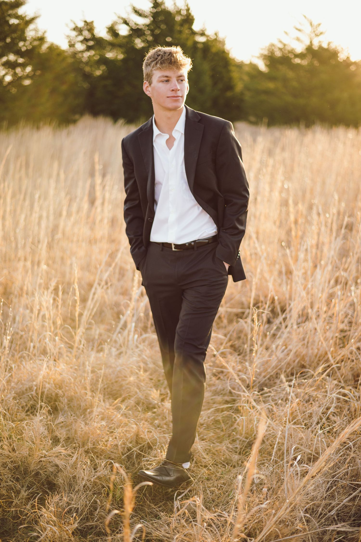 A young man in a suit poses in a golden field at sunset.