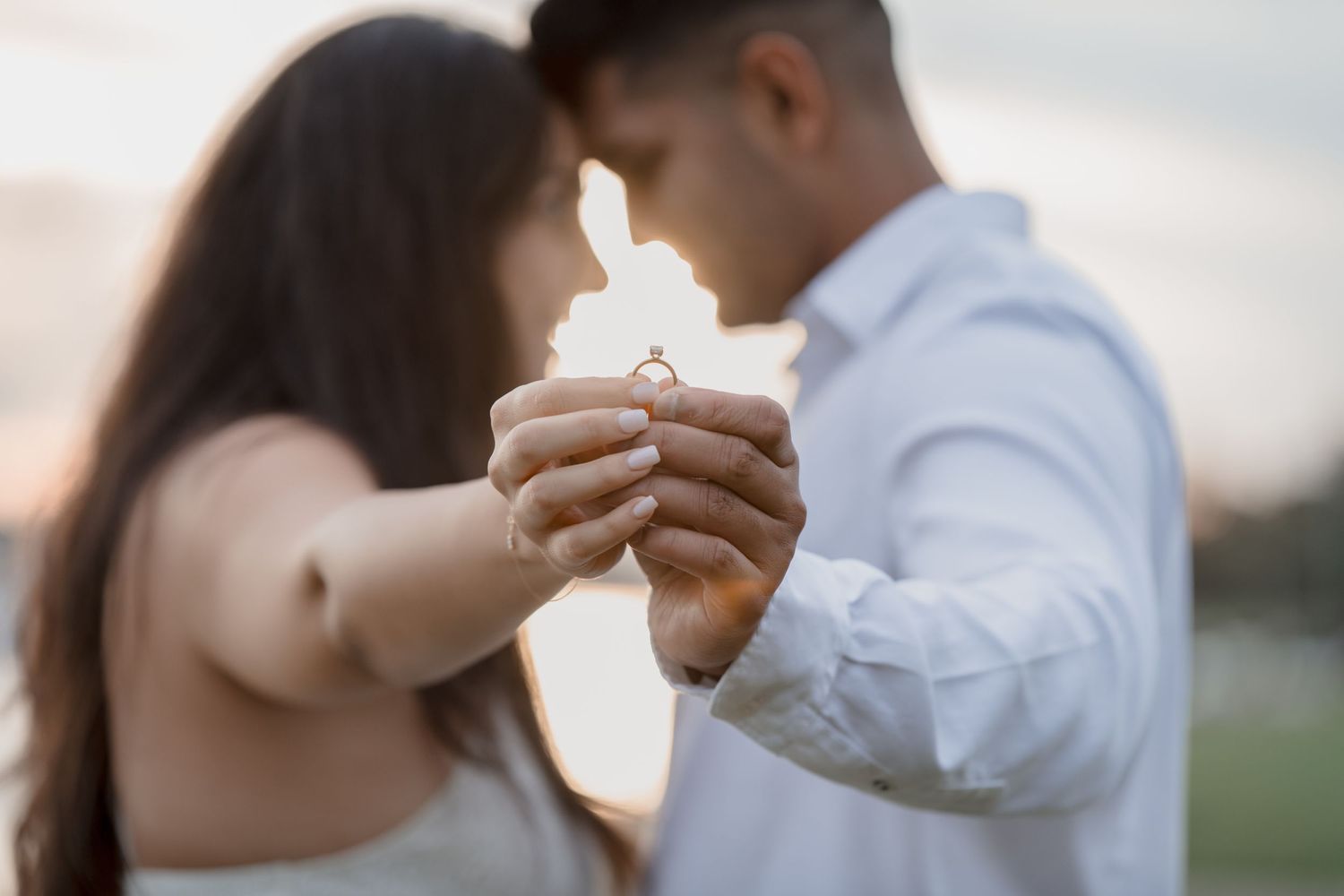 Indian couple in the background with foreheads touching out of focus holding a ring in focus in front of them in Sydney
