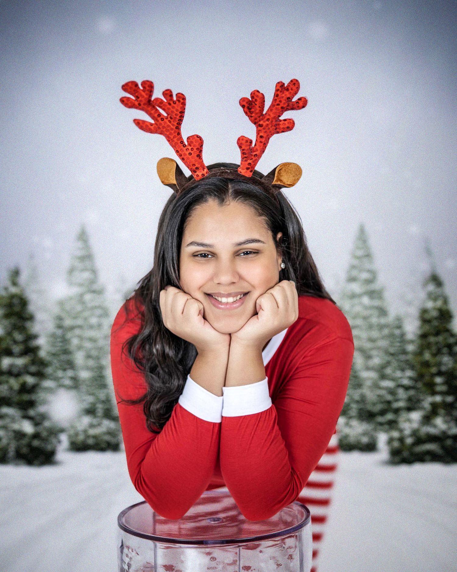 Winter portrait with reindeer antlers and red sweater against snowy evergreen background.