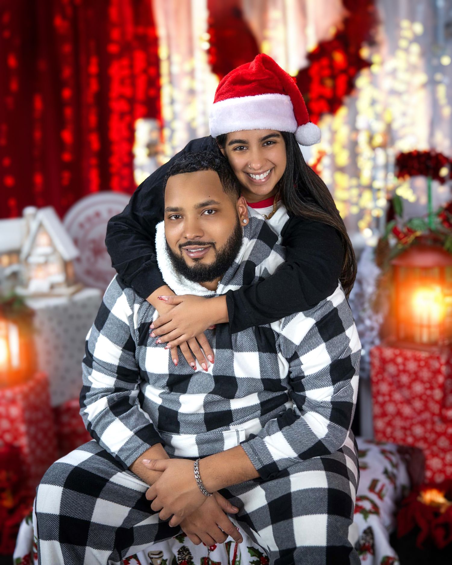 Couple in matching buffalo plaid outfits posing with Christmas decorations and lights.