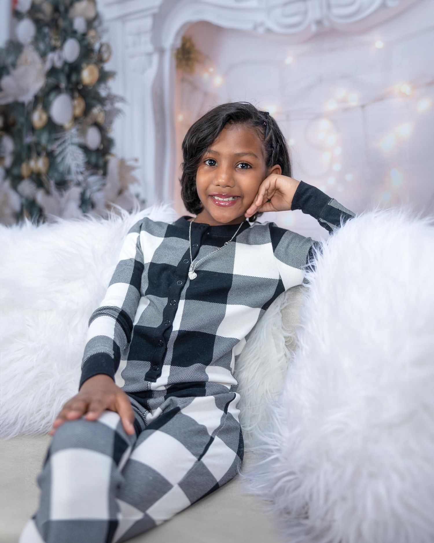 Christmas portrait featuring buffalo plaid outfit against white and sparkly holiday backdrop.