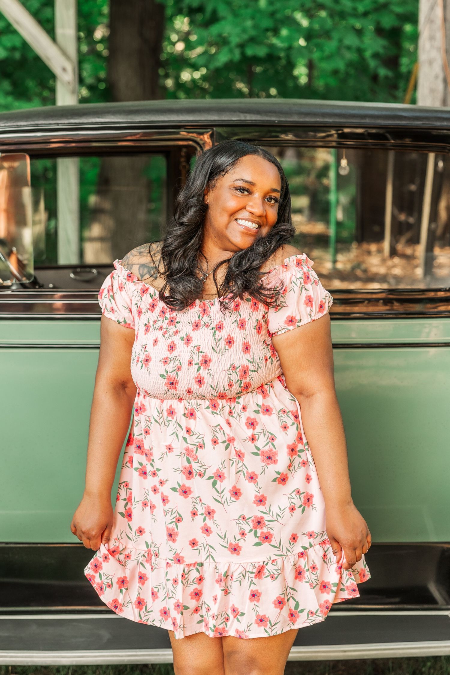 A floral print dress is styled against a vintage green car in an outdoor garden setting.