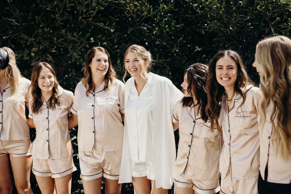 Group of bridesmaids wearing matching light colored outfits posing together.