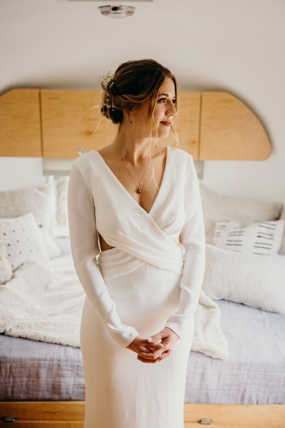 Elegant long-sleeved white wedding dress shown against soft bedroom decor.