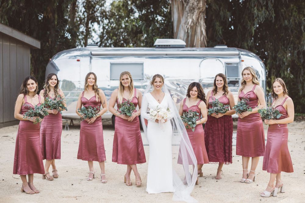 Wedding party in burgundy and white attire poses for group photos on a sunny day.