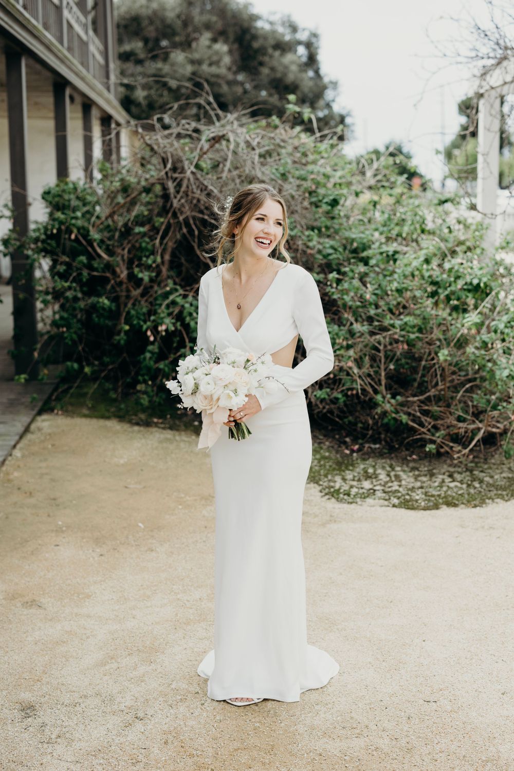 Elegant white wedding dress with long sleeves photographed in outdoor garden setting.
