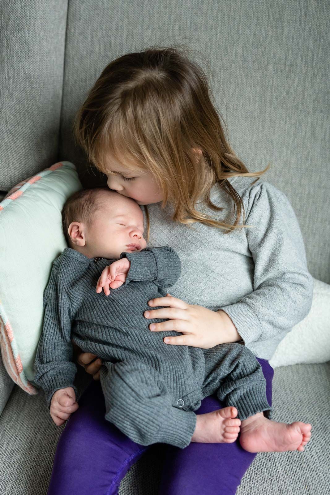 Sister kissing newborn baby brother at home.