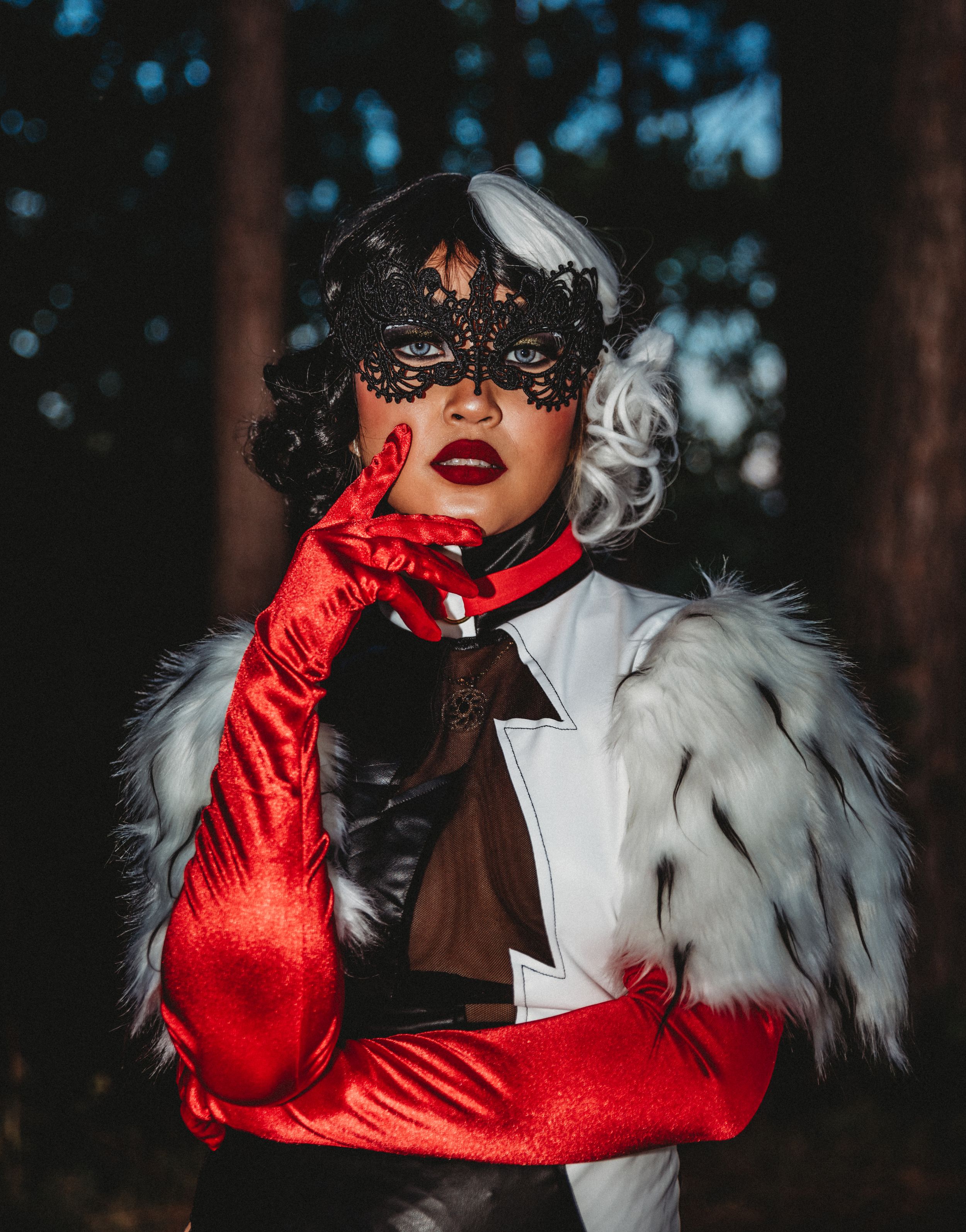 Dramatic portrait featuring a black and white fur coat, red gloves, and lace mask in a forest.