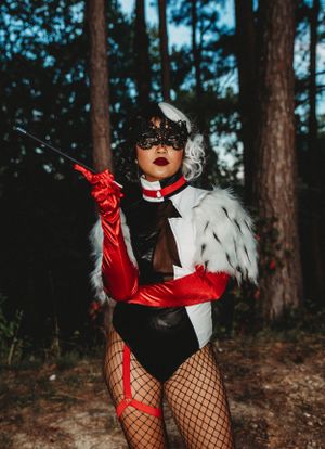 Stylized Cruella de Vil cosplay with red gloves and spotted fur coat in a wooded setting.