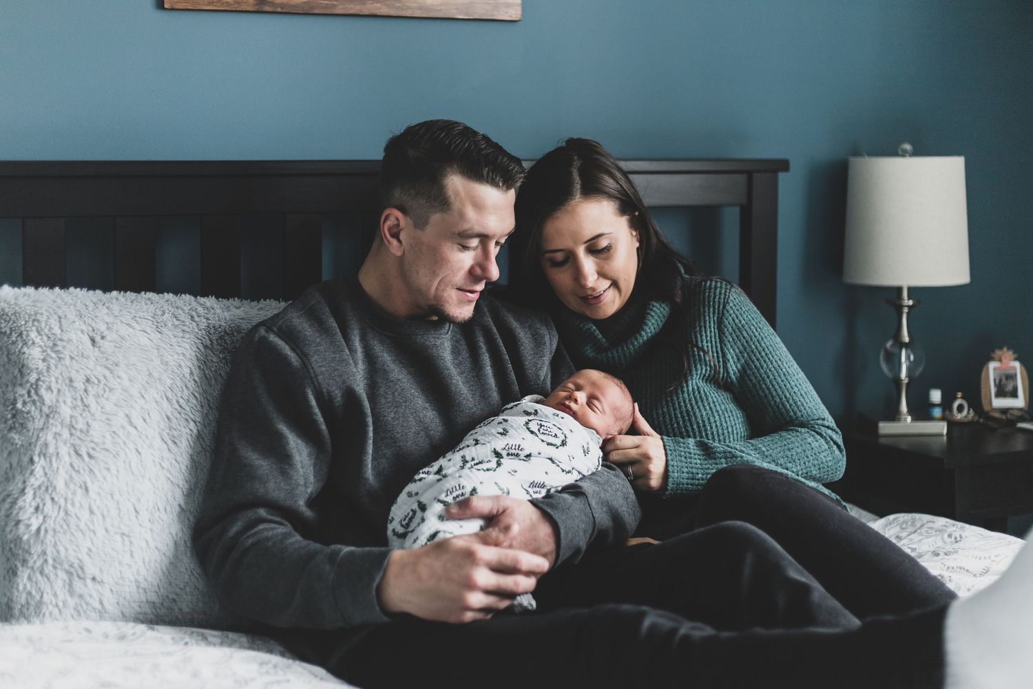 a shot of new parents sitting on their bed holding their newborn baby boy