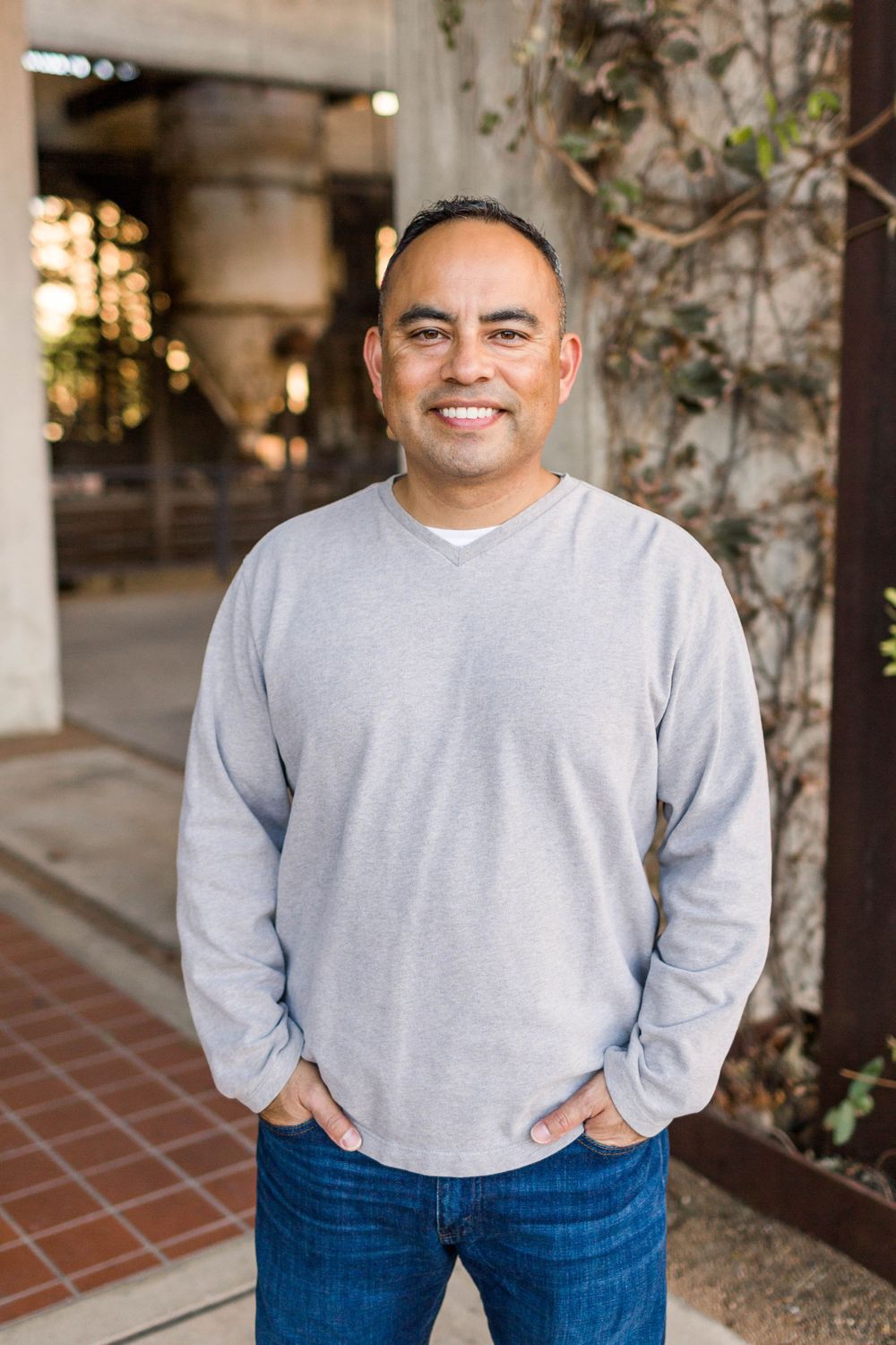 Portrait of person in grey sweater with warm lighting and architectural elements in background.
