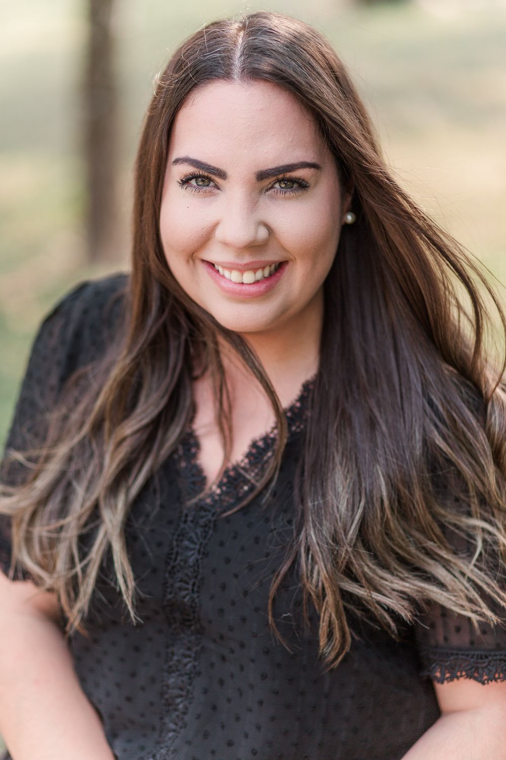 Close-up portrait of someone in black lace dress with long brown hair outdoors.