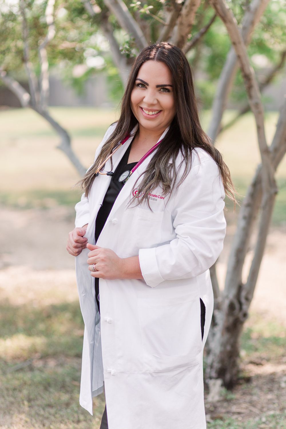 Professional portrait of medical practitioner in white coat outdoors with trees in background.