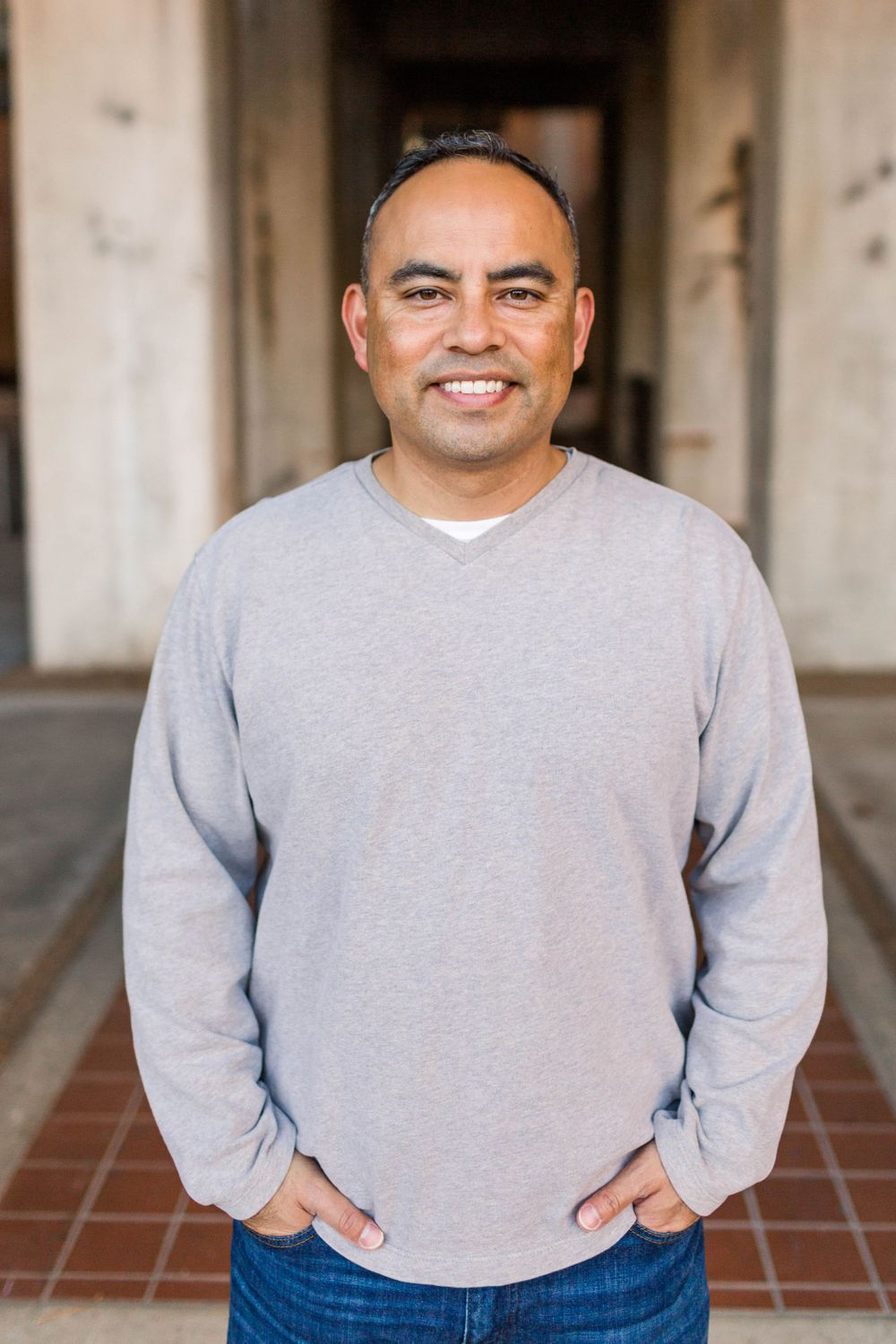 Casual portrait of person wearing light grey sweater against architectural backdrop.