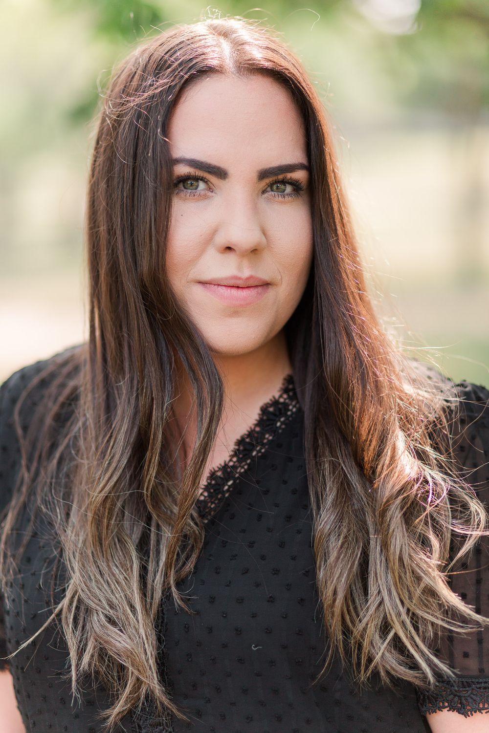 Person wearing black lace top smiling at camera with long brown ombre hair.