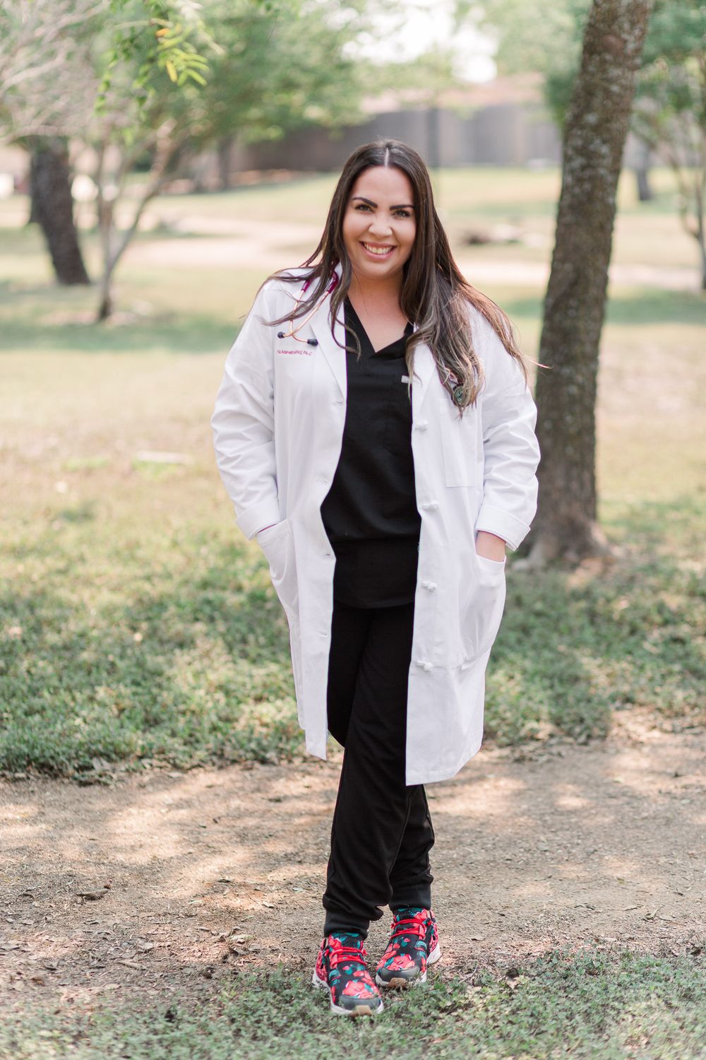 Healthcare professional in white coat and colorful sneakers standing outdoors in a natural setting.