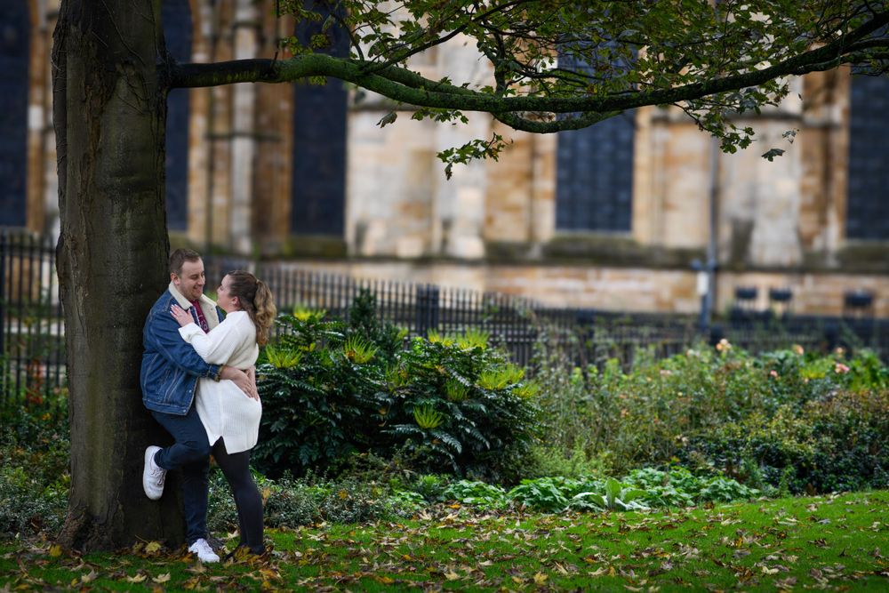 Romantic couple sharing tender moment under tree with cathedral in background.