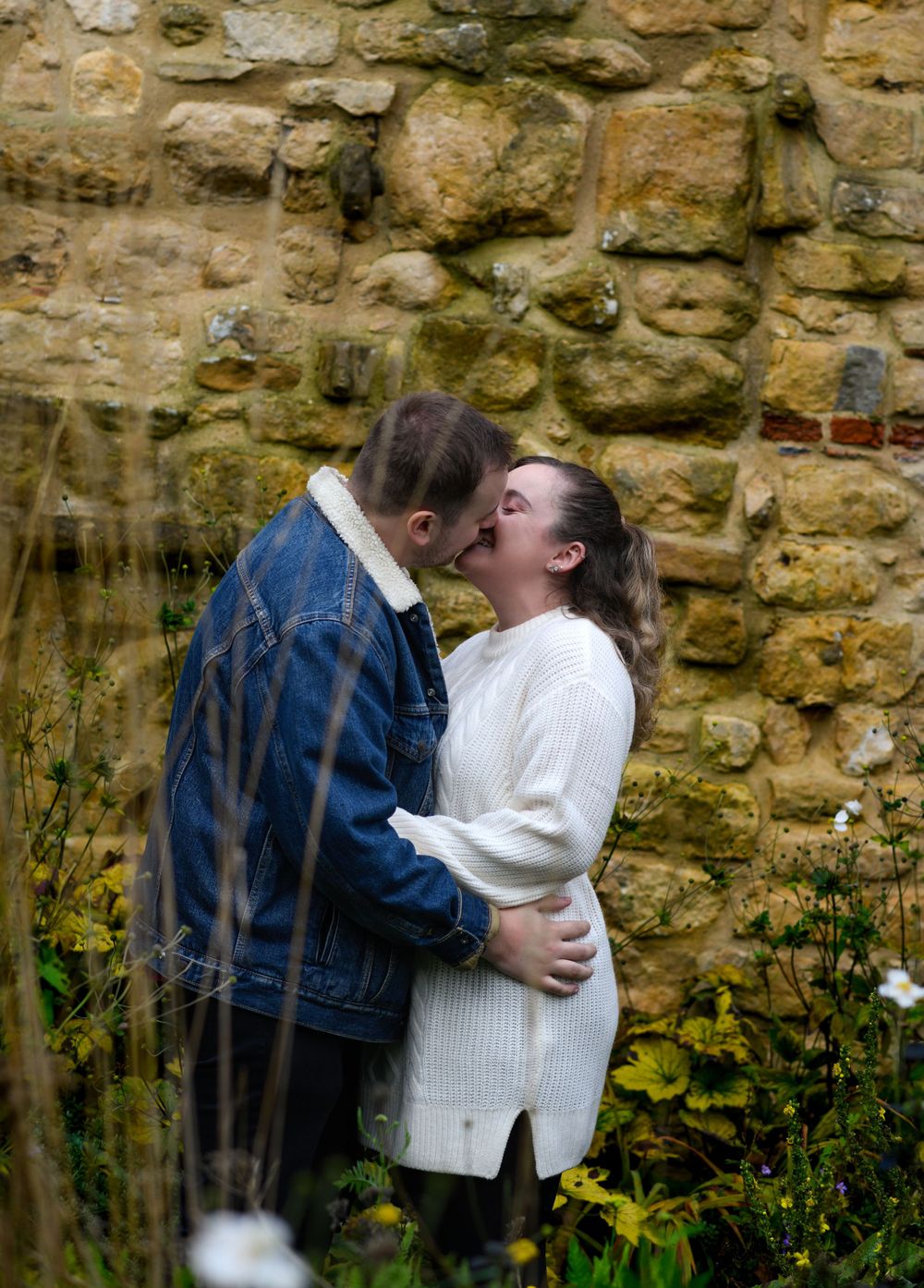 Intimate couple moment captured against textured stone wall with wildflowers.