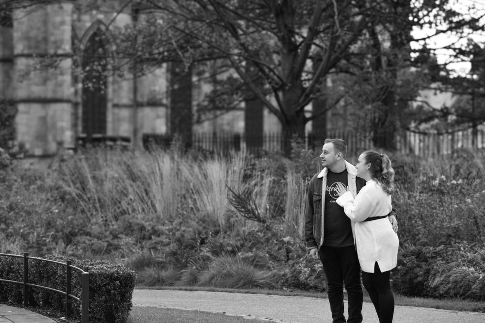 Black and white photo of couple walking along garden path near historic architecture.
