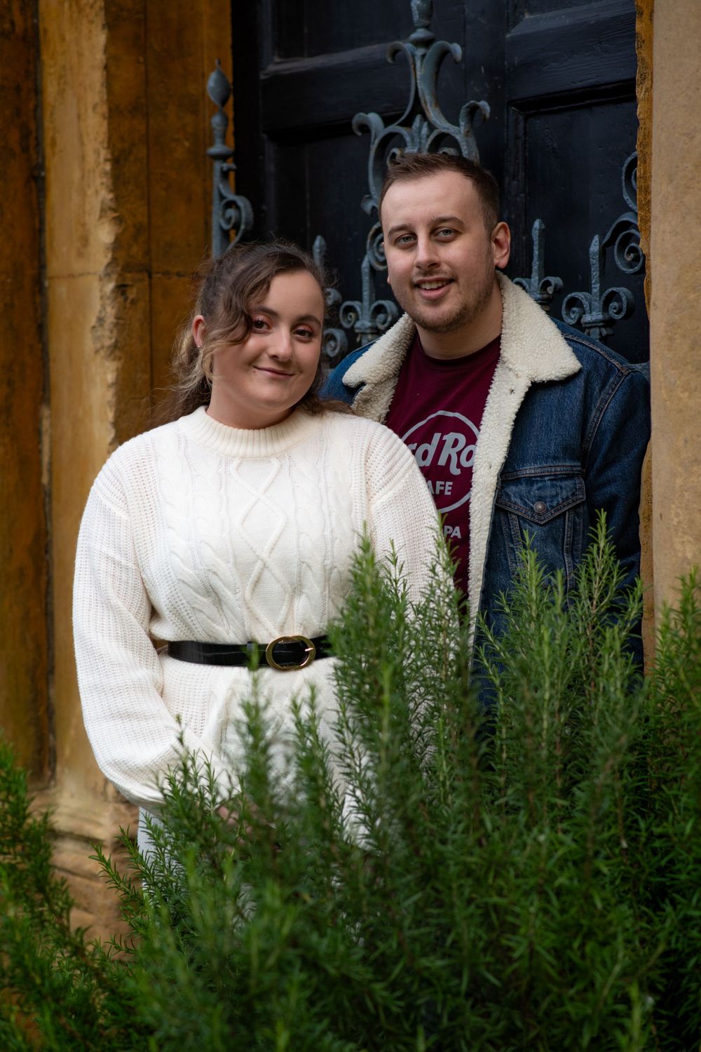 Romantic couple poses by ornate iron doorway wearing coordinated white and denim outfits.