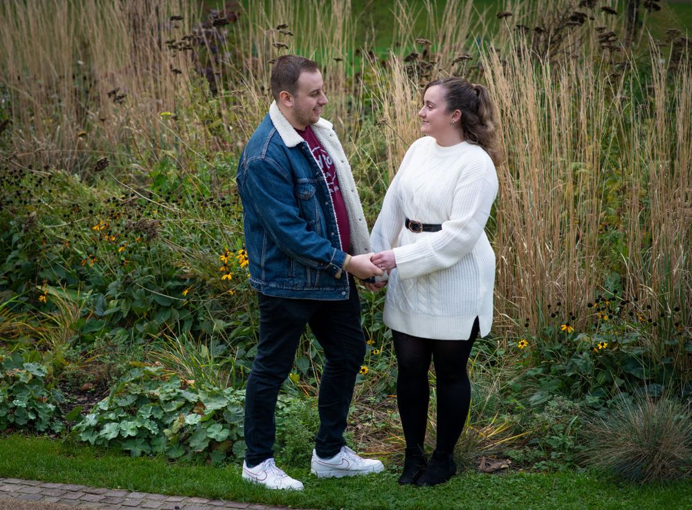 Couple poses together among tall reeds with historic building in background.