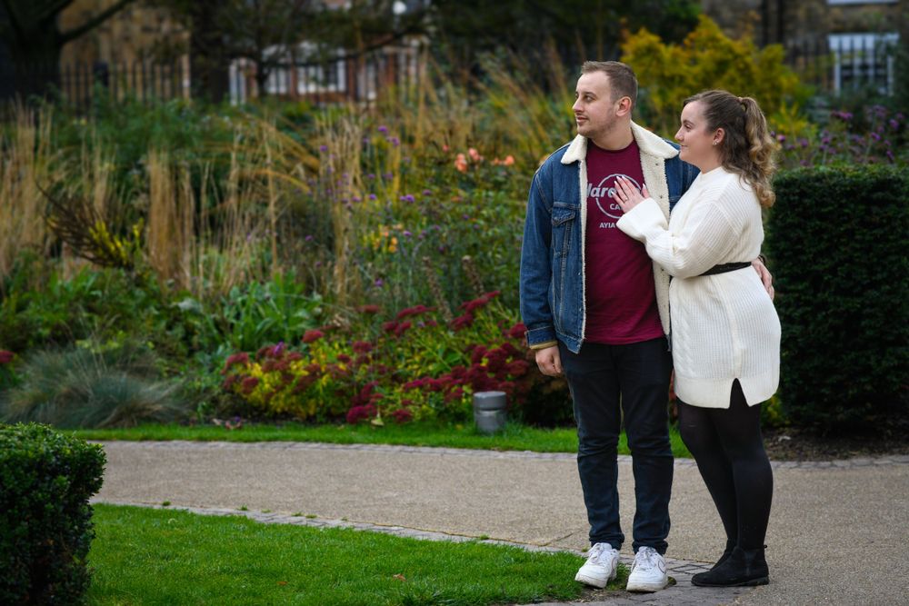 Couple walking together in garden path with manicured hedges and autumn foliage.