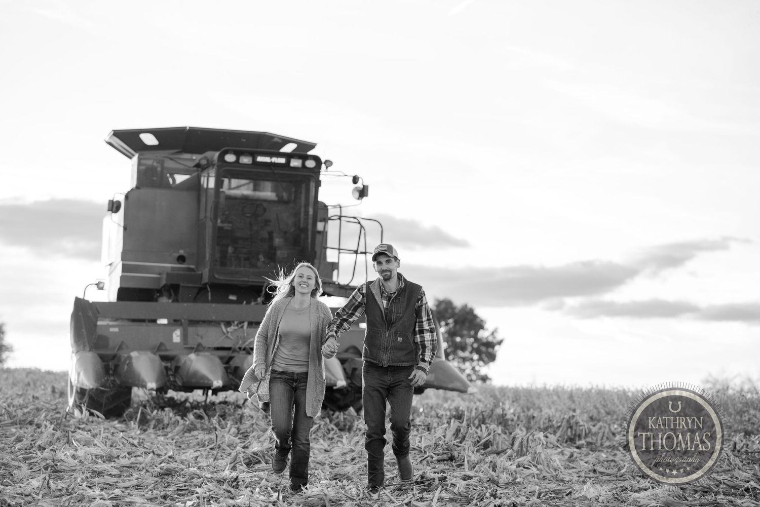 A couple walks together through a field with combine harvester behind them in black and white.