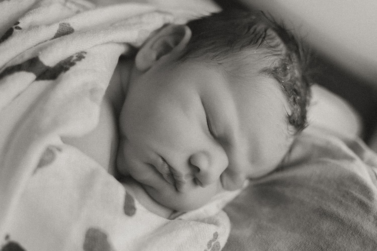 Black and white portrait of a sleeping newborn baby wrapped in a soft patterned blanket.
