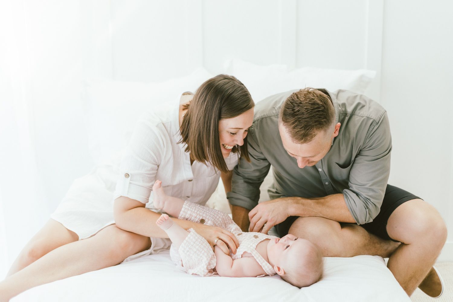 Family enjoying tender moment together on white bedding while reading a book.