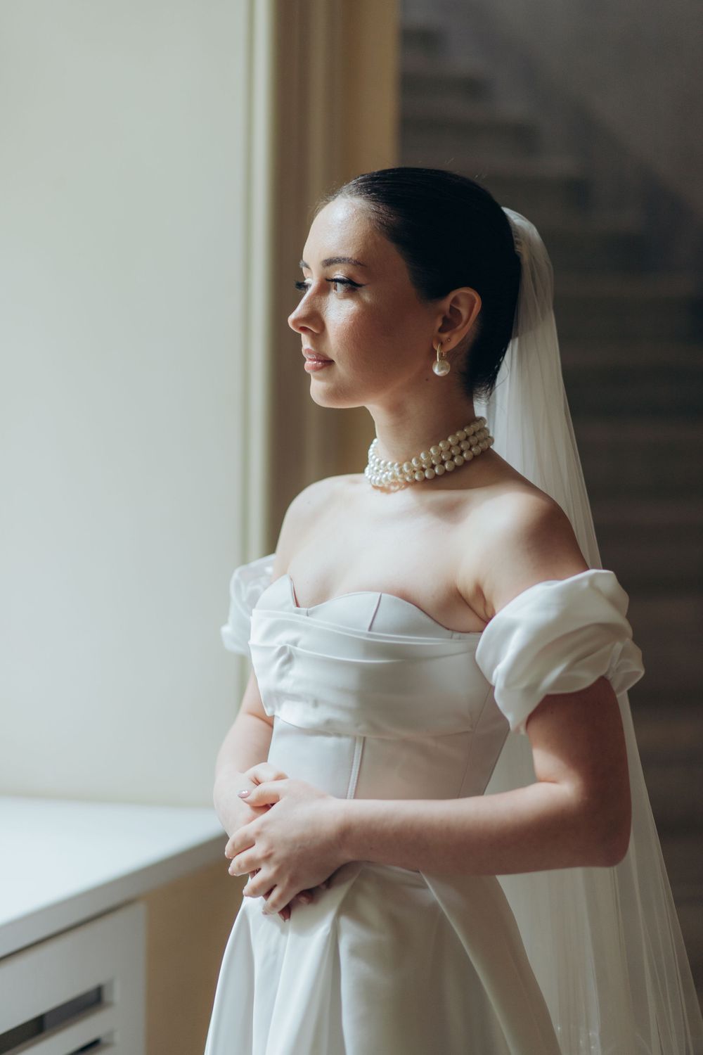Classic bridal portrait featuring pearl necklace and off-shoulder gown in natural window lighting.
