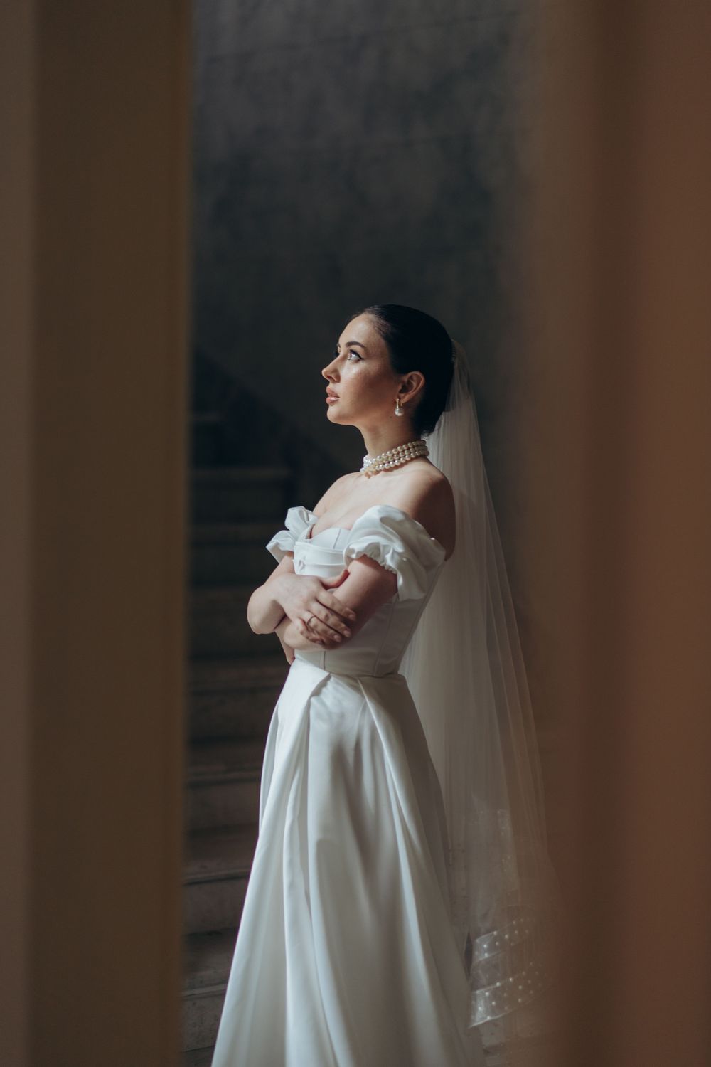 Elegant off-shoulder wedding dress with puff sleeves and flowing train captured in dramatic window light.