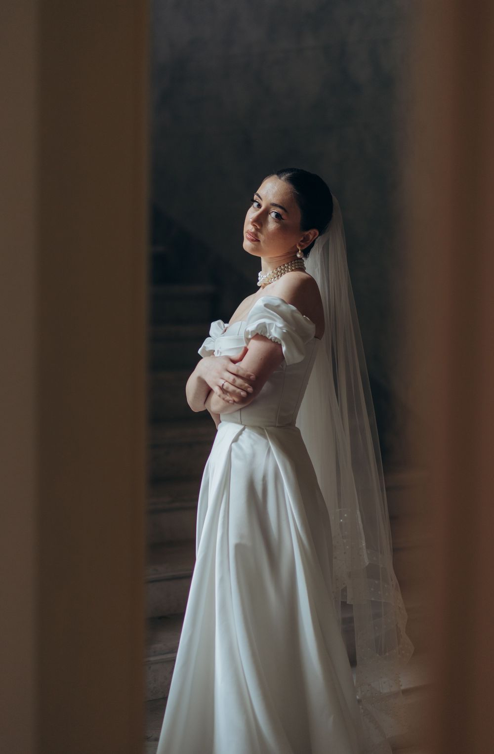 Romantic side profile of bride in classic white gown against dark background.