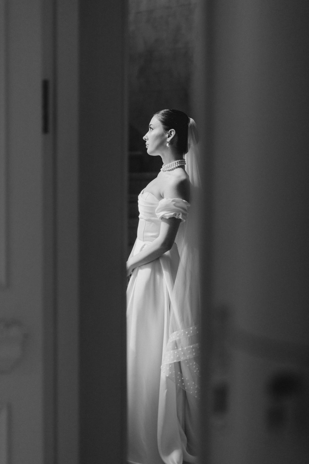 Dramatic black and white portrait of bride in structured gown with flowing veil.