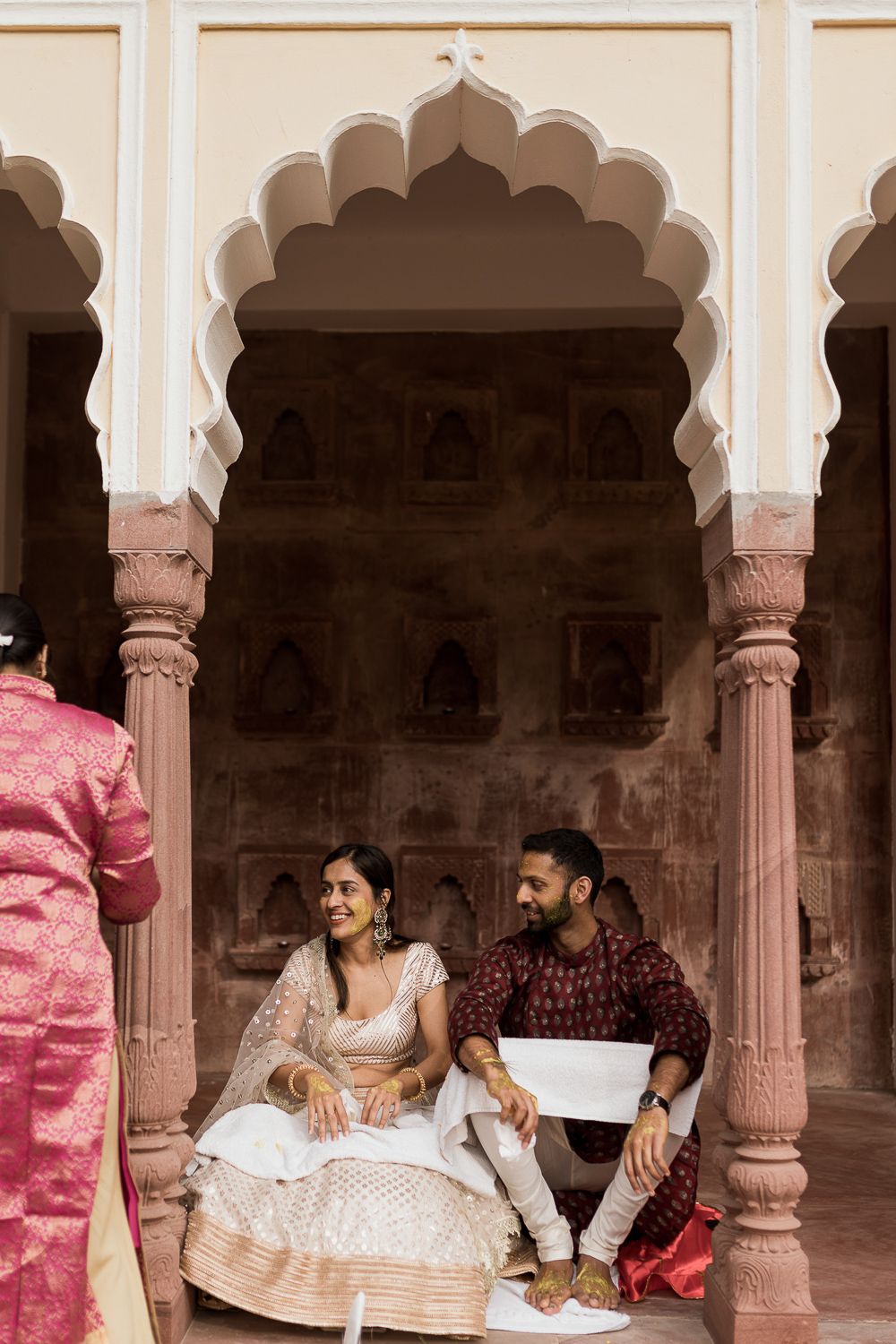 Couple seated under ornate archway in traditional Indian palace architecture.