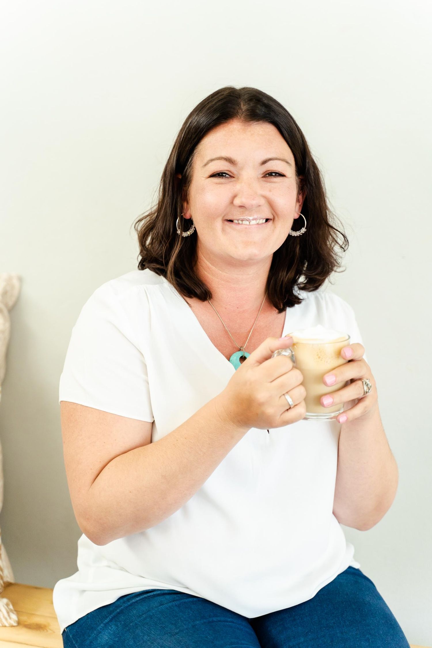 Person in white t-shirt holding coffee mug against minimalist background.