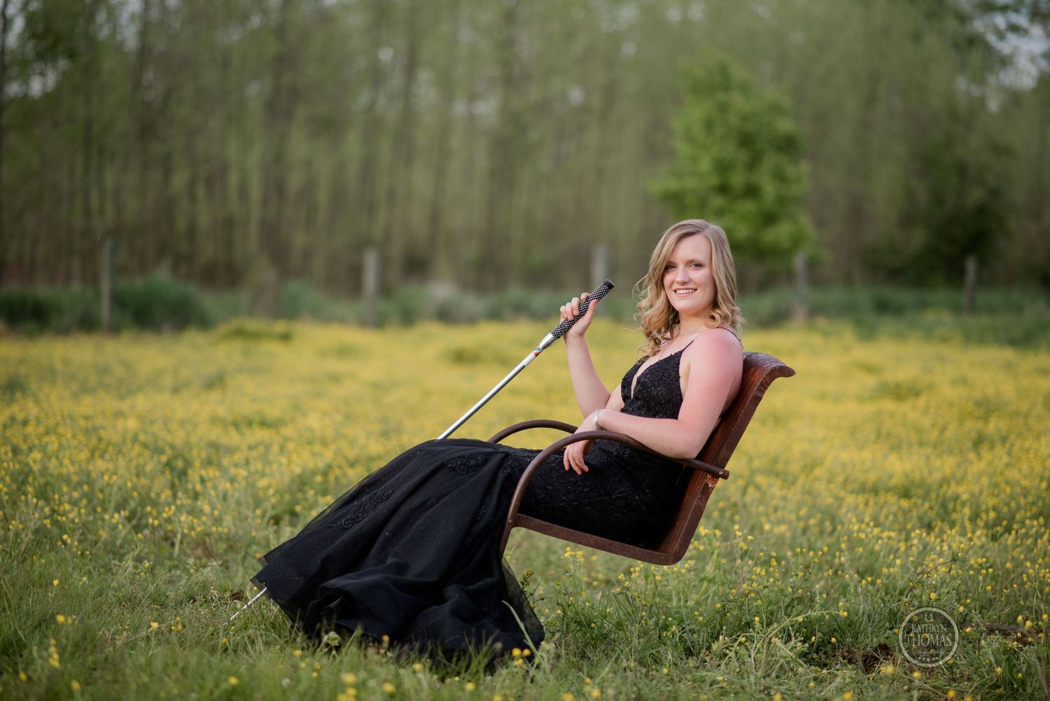 A relaxed portrait in a black formal dress while seated in a chair among yellow wildflowers.