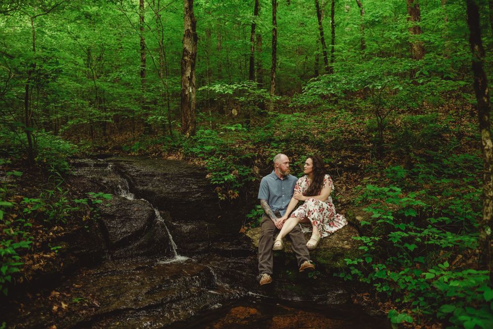 A romantic moment captured on moss-covered rocks in a lush green forest setting.
